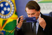 O presidente Jair Bolsonaro tenta colocar  máscara durante evento